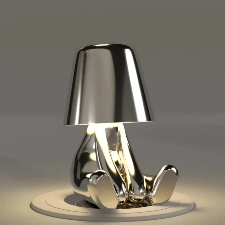 Designerska lampka stołowa z postacią ludzką i kloszem LED w srebrnym kolorze