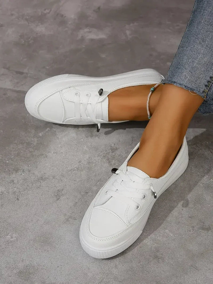 Sneakersy Damskie Sznurowane białe z okrągłym noskiem i płaską podeszwą z bieżnikiem na modelce w szarych spodniach