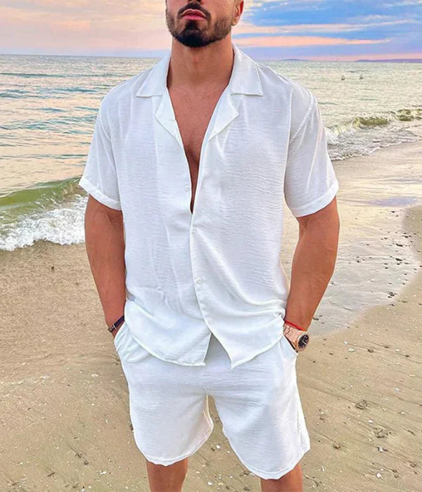 Stanisław prezentuje Męski Letni Zestaw z Teksturowanym Wykończeniem w białym kolorze na plaży — koszula z krótkim rękawem i szorty